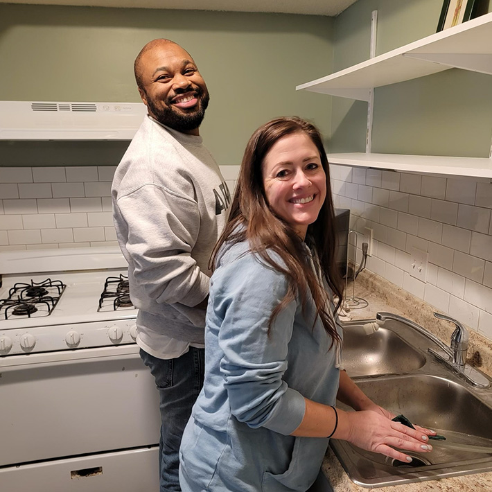 Two smiling people washing dishes in a kitchen.