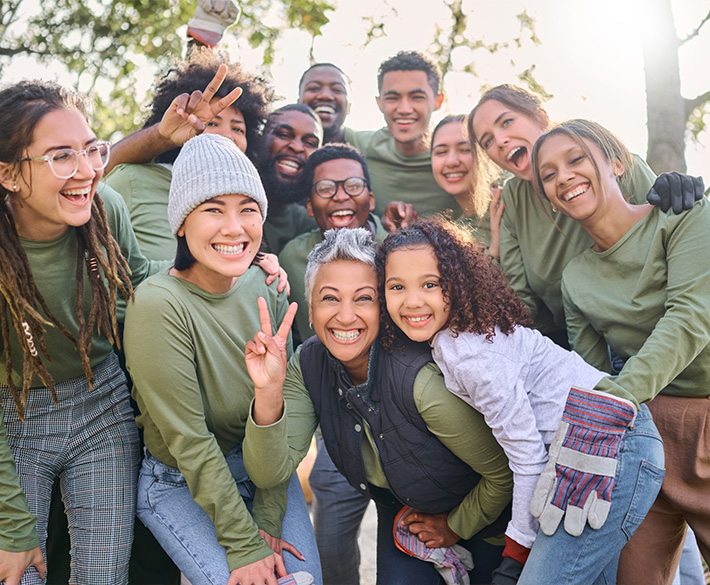 A happy group of people in matching olive green long sleeve t-shirts, smile with work gloves on