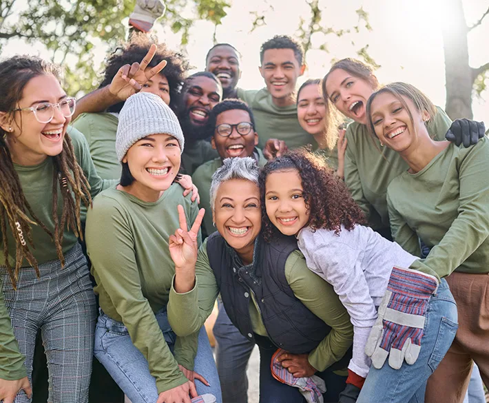 A happy group of people in matching olive green long sleeve t-shirts, smile with work gloves on