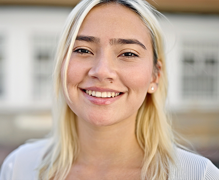 A close-up photo of a woman with blonde hair and brown eyes smiles