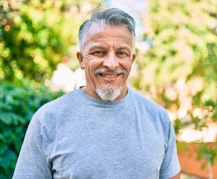 A man with gray hair, goatee and earring smiles in a gray t-shirt.