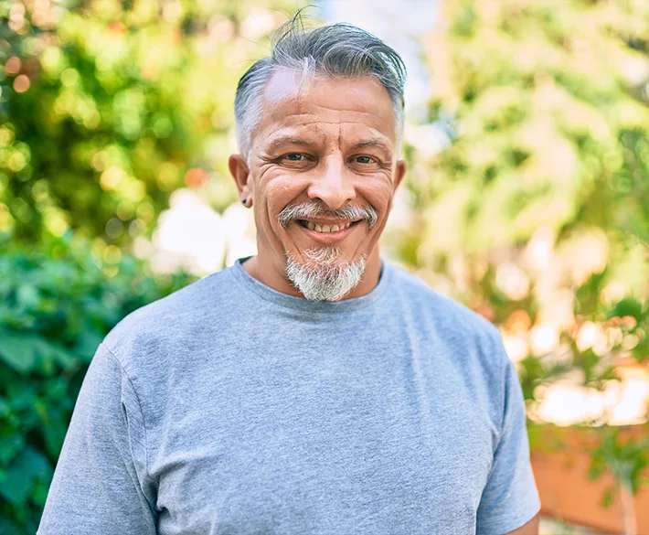 A man with gray hair, goatee and earring smiles in a gray t-shirt.