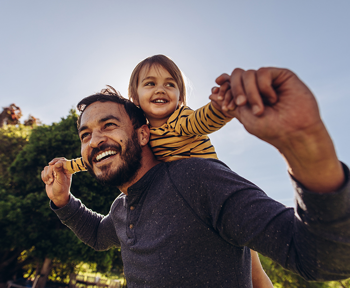 A little girl rides on the back of her dad through the park