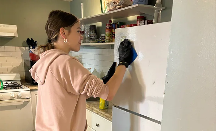 A girl works on wiping down a refrigerator with a sponge