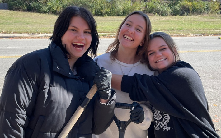 Three girls hugging and laughing as they do yard work.